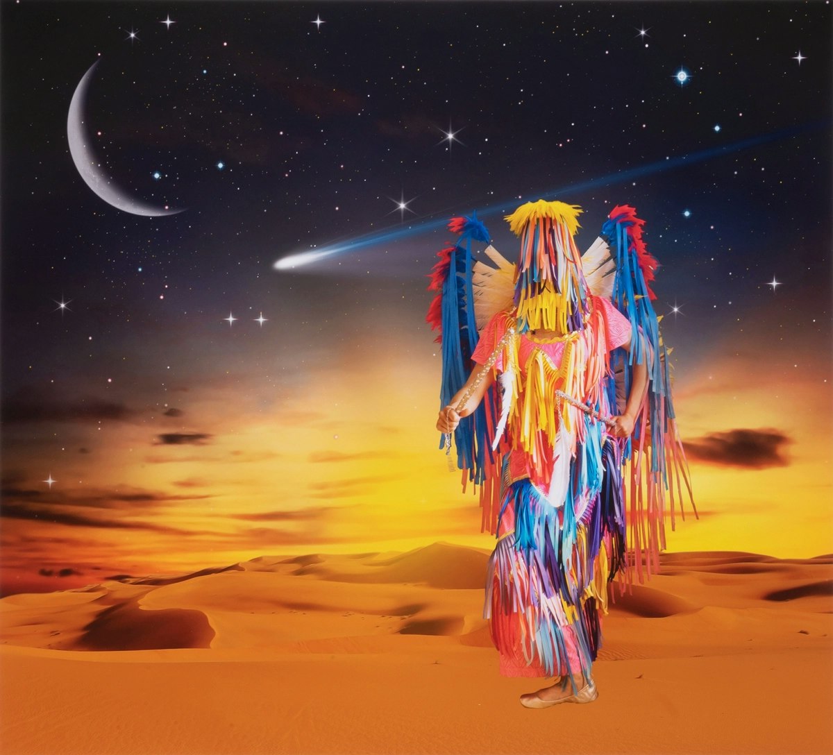 Person wearing bright, colorful Native regalia, stands against a sandy desert landscape with a starry sky, a large crescent moon, and a shooting star.
