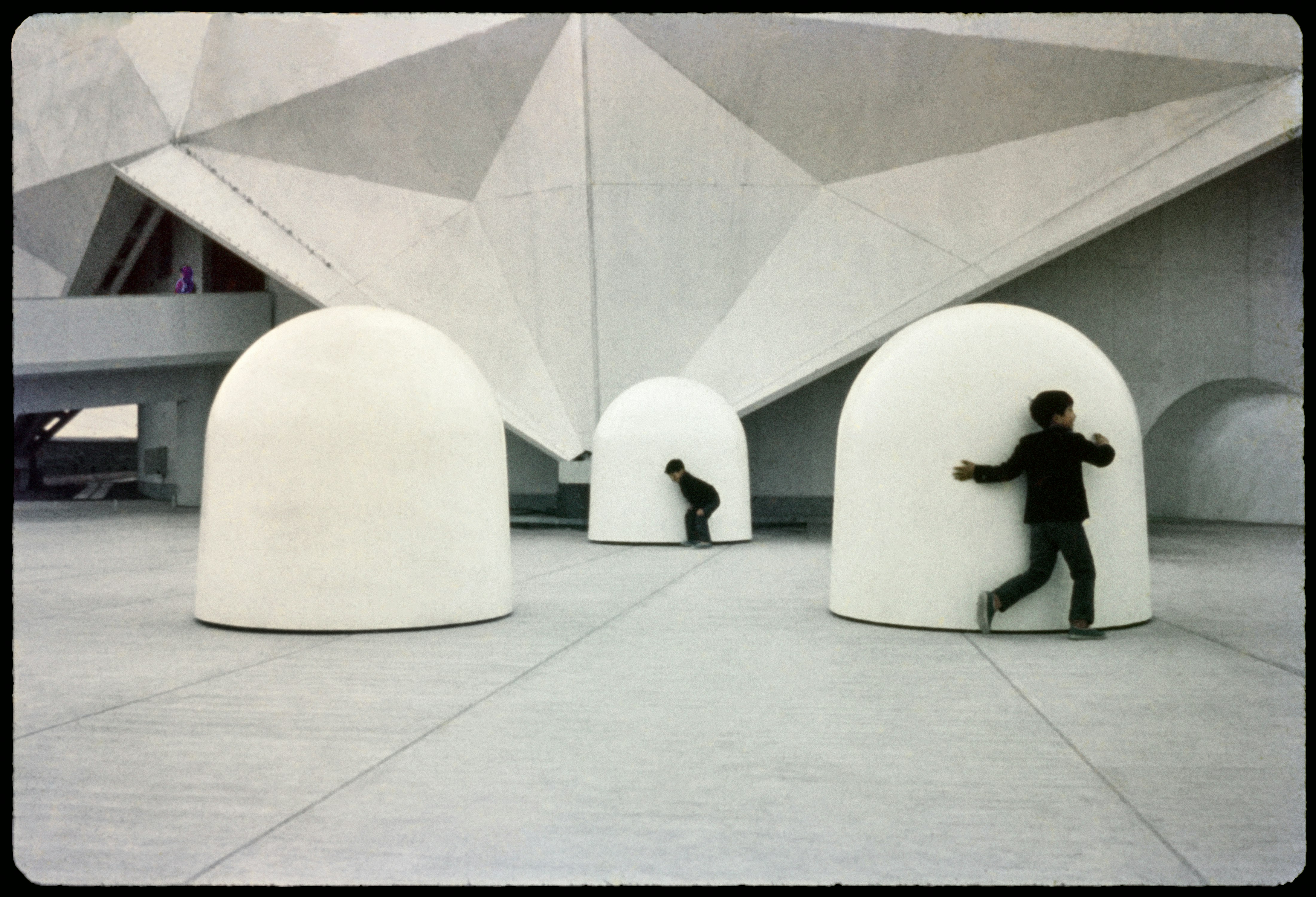 A photograph of large white domes on a concrete floor. Two figures in black crouch in front of two of the domes.