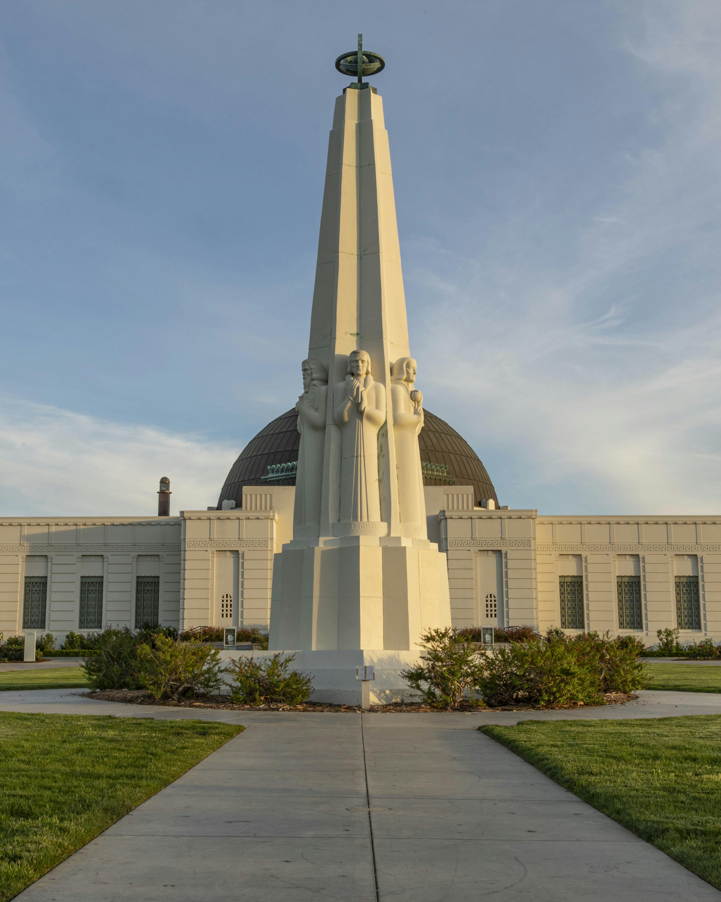 Exterior view of the Griffith Observatory, with a large outdoor concrete sculpture of a group of six people on all sides of the monument.