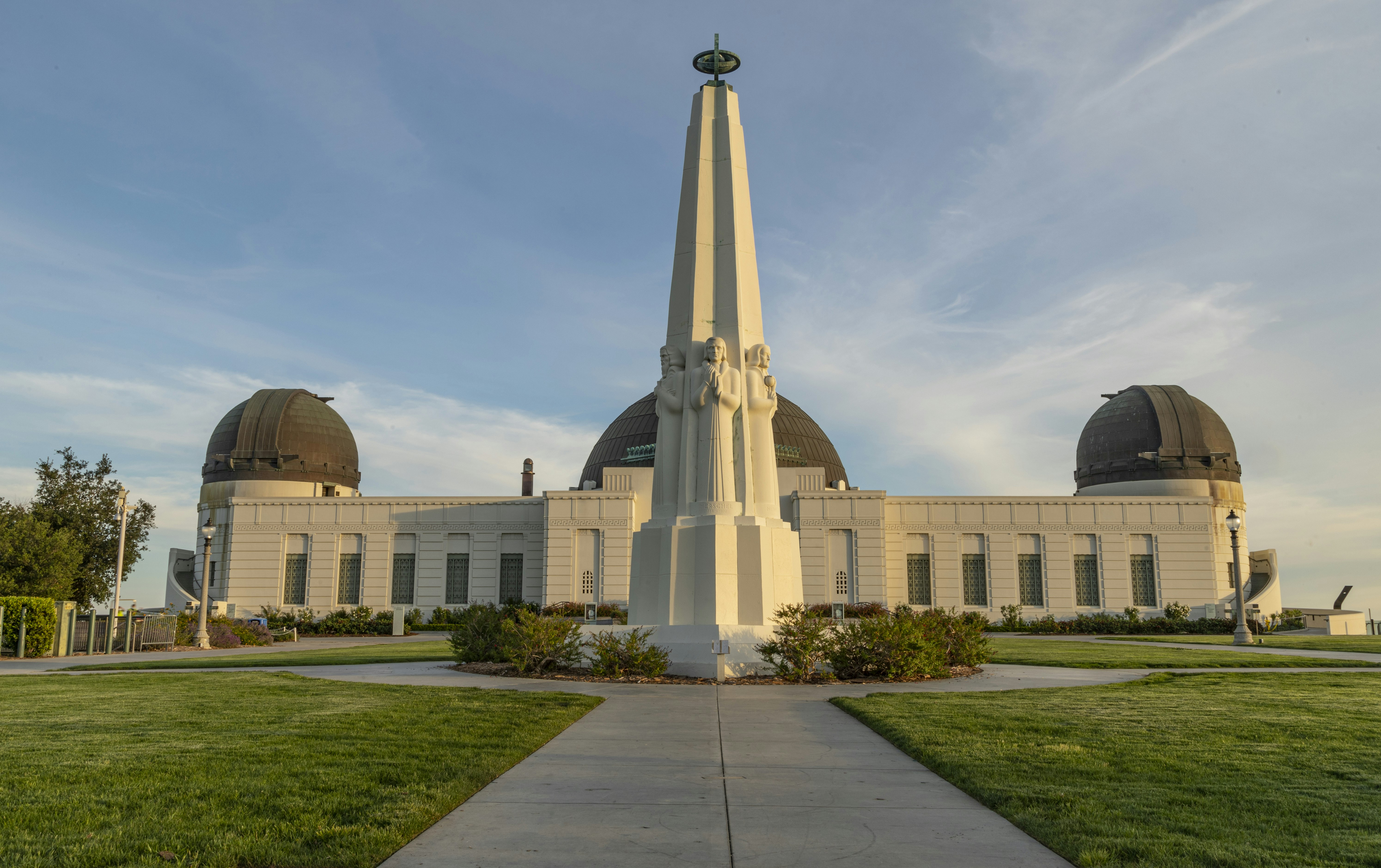 Exterior view of the Griffith Observatory, with a large outdoor concrete sculpture of a group of six people on all sides of the monument.