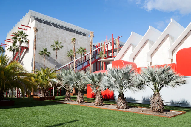 A photograph of a white building with red accents and palm trees surrounding it.