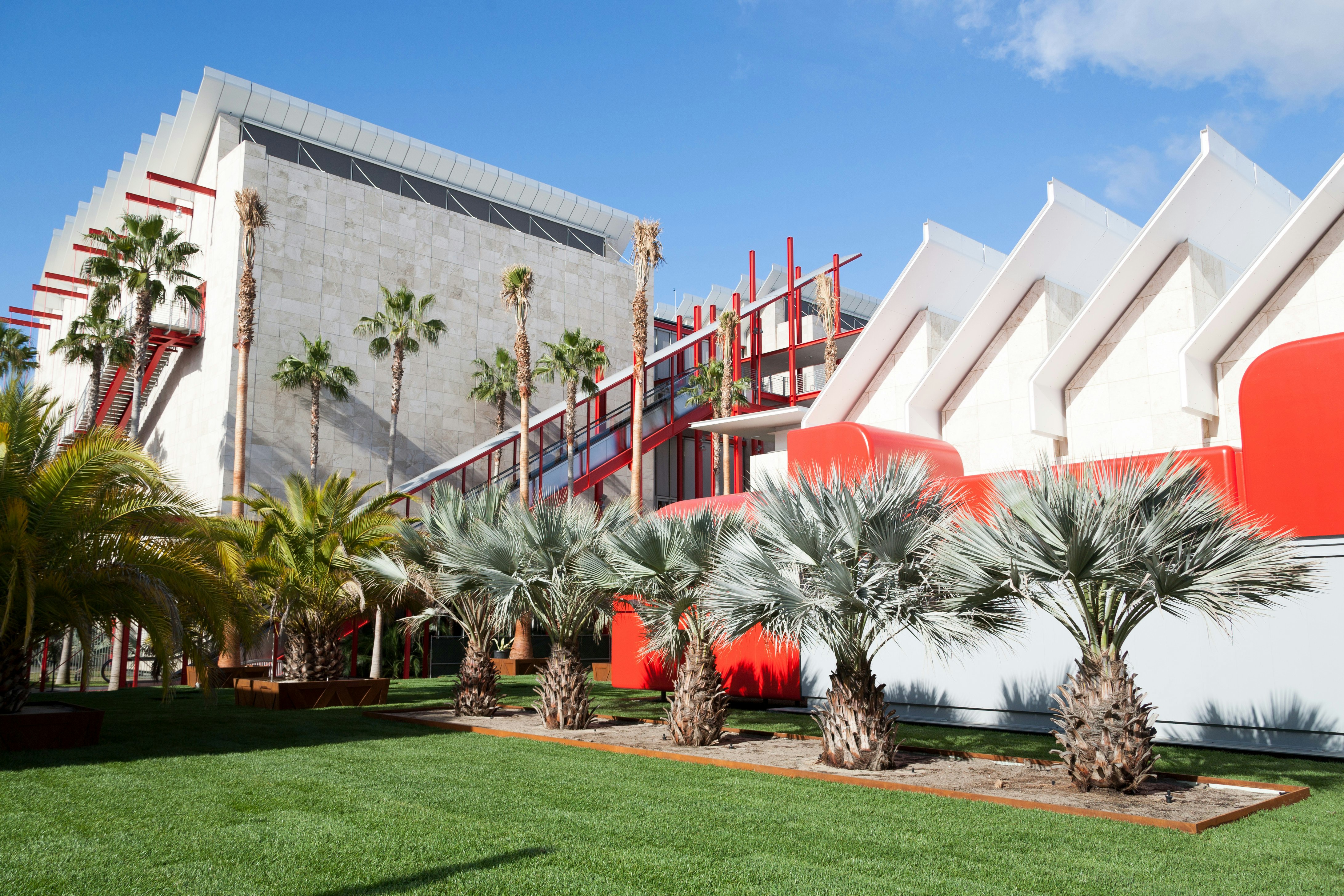 A photograph of a white building with red accents and palm trees surrounding it.