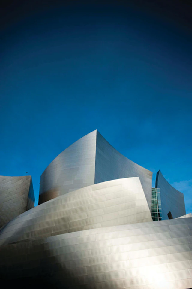 Photo of silver metal building with organic forms against a clear blue sky.