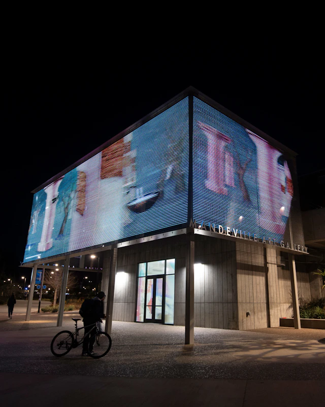 Photograph of a rectangular building at night. The top half of the building has an illuminated projection of purple abstract shapes on a blue background.