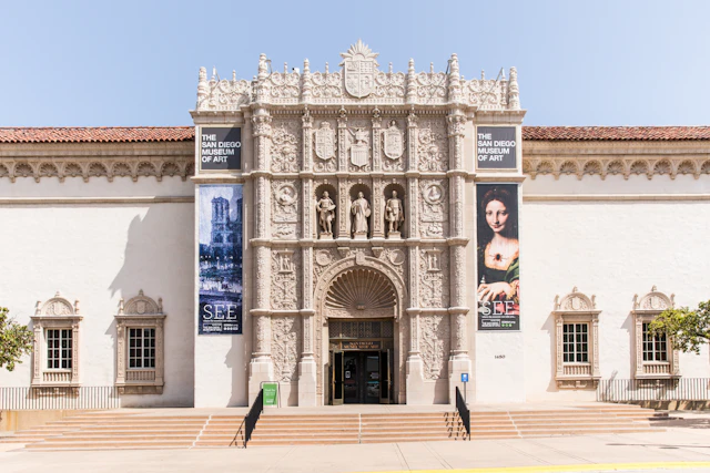 A photograph of a pale yellow stone building with ornate carvings on the facade. Steps lead up to the entrance doors.